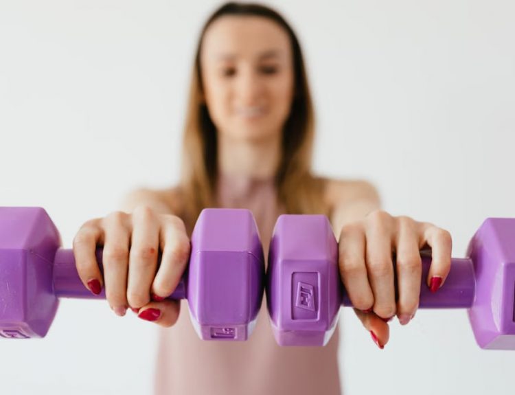 Defocused content young female doing bicep exercise with dumbbells during functional training in light studio